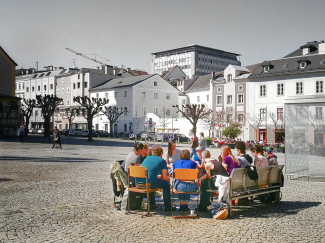 Menschen sitzen im Sesselkreis auf öffentlichem Platz